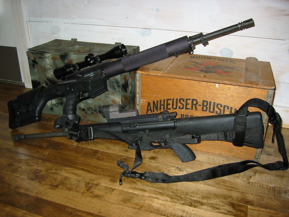 Two rifles with scopes and slings resting on a wooden floor in front of ammo crates