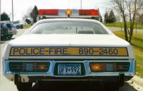 1991 Ford Crown Victoria - This older model police car has a light bar on top and a phone number on its rear.