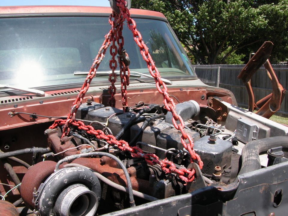 Engine being hoisted from red vintage Ford truck with red chains
