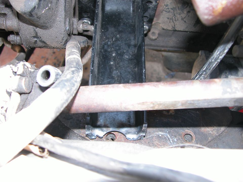 Grimy engine bay close-up of a black valve cover crossed by a rusty linkage rod