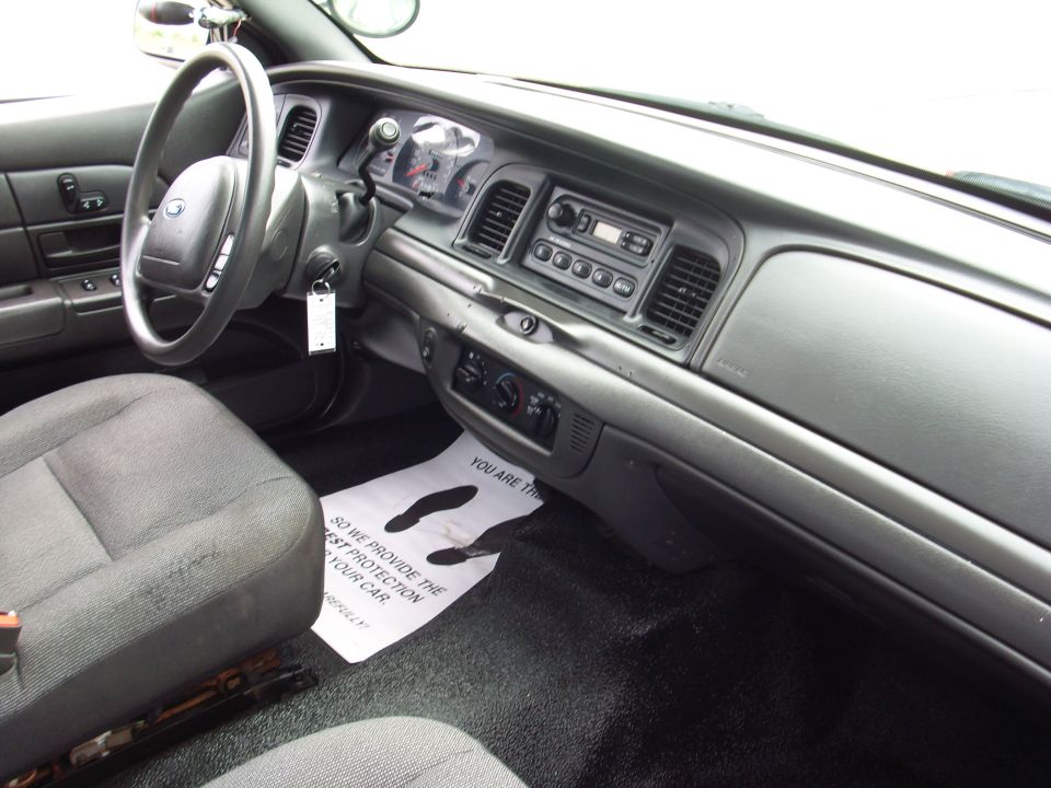 2004 Ford Crown Victoria interior showing dashboard, steering wheel, and seats. Floor mat has text and footprints