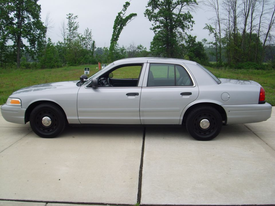 Silver 2004 Ford Crown Victoria sedan, side view, black wheels, parked on concrete