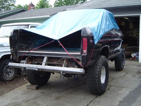 1979 Ford Bronco - A black 1979 Ford Bronco is parked in a driveway, its bed covered by a blue tarp.