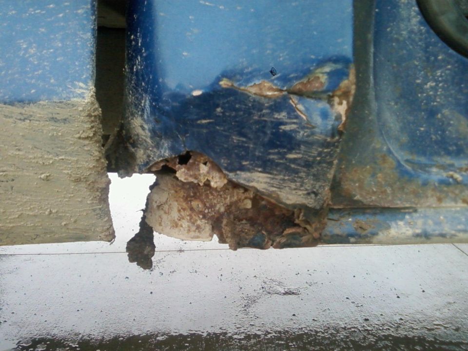 Rust hole and corrosion at lower corner of blue vehicle body panel