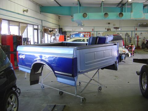 1996 Ford F-250 - A blue and silver pickup truck bed, likely from a 1996 Ford F-250, is elevated on a rolling stand inside a workshop.