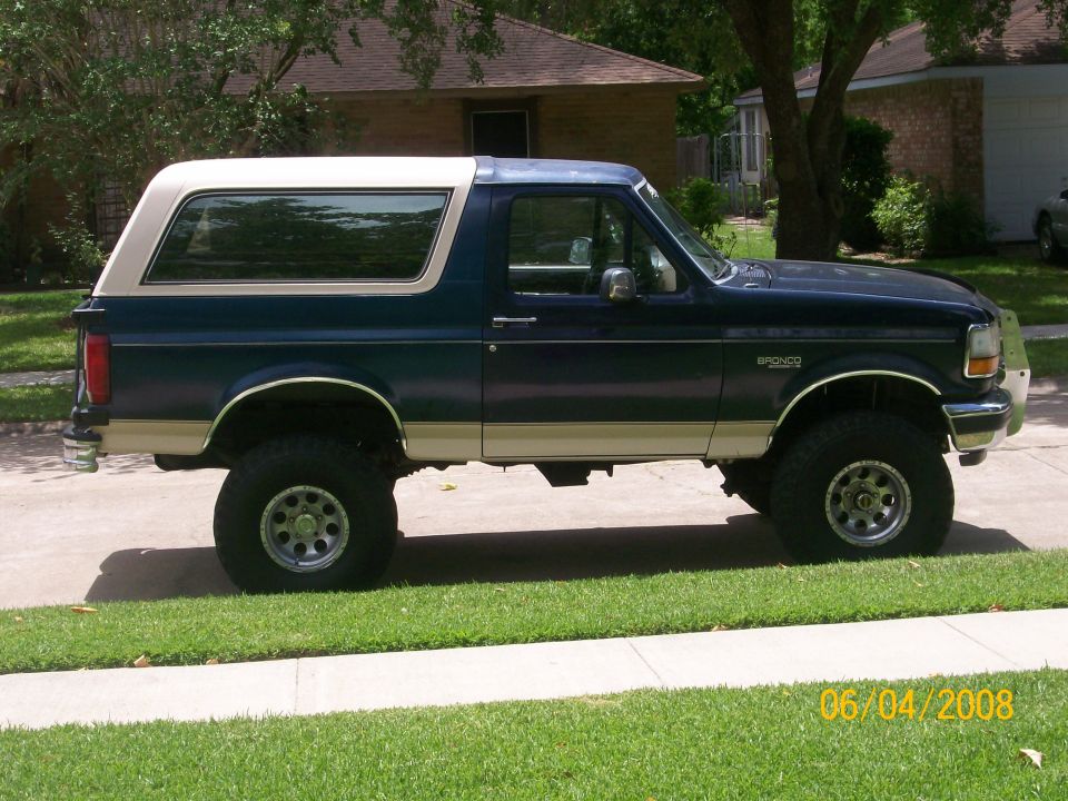 1992 Ford Bronco, dark blue with tan stripe and white top, lifted suspension, side view