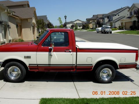 1988 Ford F-150 - A two-tone red and white Ford F-150 pickup truck is parked on a residential street with houses in the background.