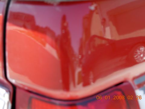 1988 Ford F-150 — Red truck bed with reflections of buildings and another vehicle. Visible timestamp and website