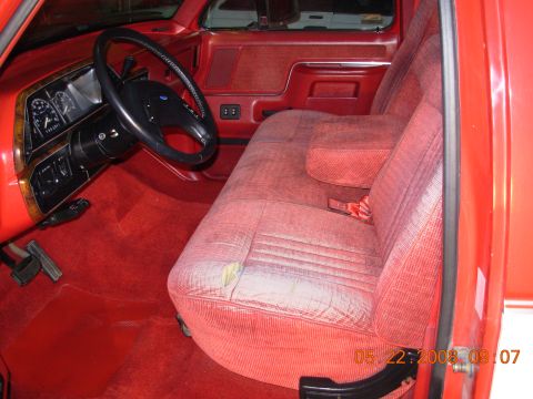 1988 Ford F-150 — Red fabric bench seat with a tear, dashboard with wood trim, and steering wheel in a truck interior
