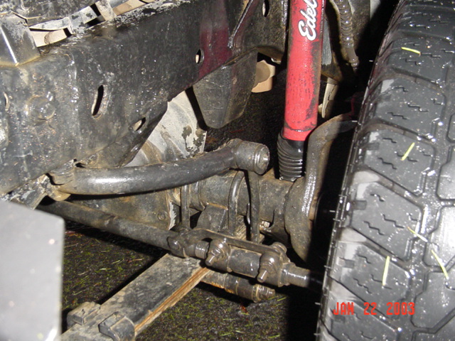 Underside view of front suspension with red Edelbrock shock, steering linkage and mud tire