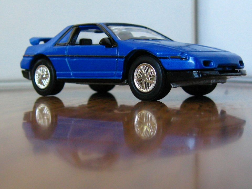Blue die-cast model 1980s sports coupe with spoiler and chrome wheels on a reflective surface