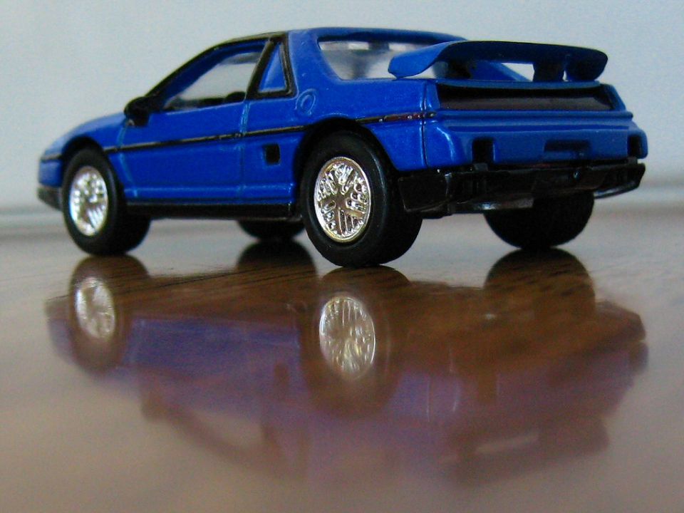 Blue die-cast Pontiac Fiero model with rear spoiler on a polished wood table