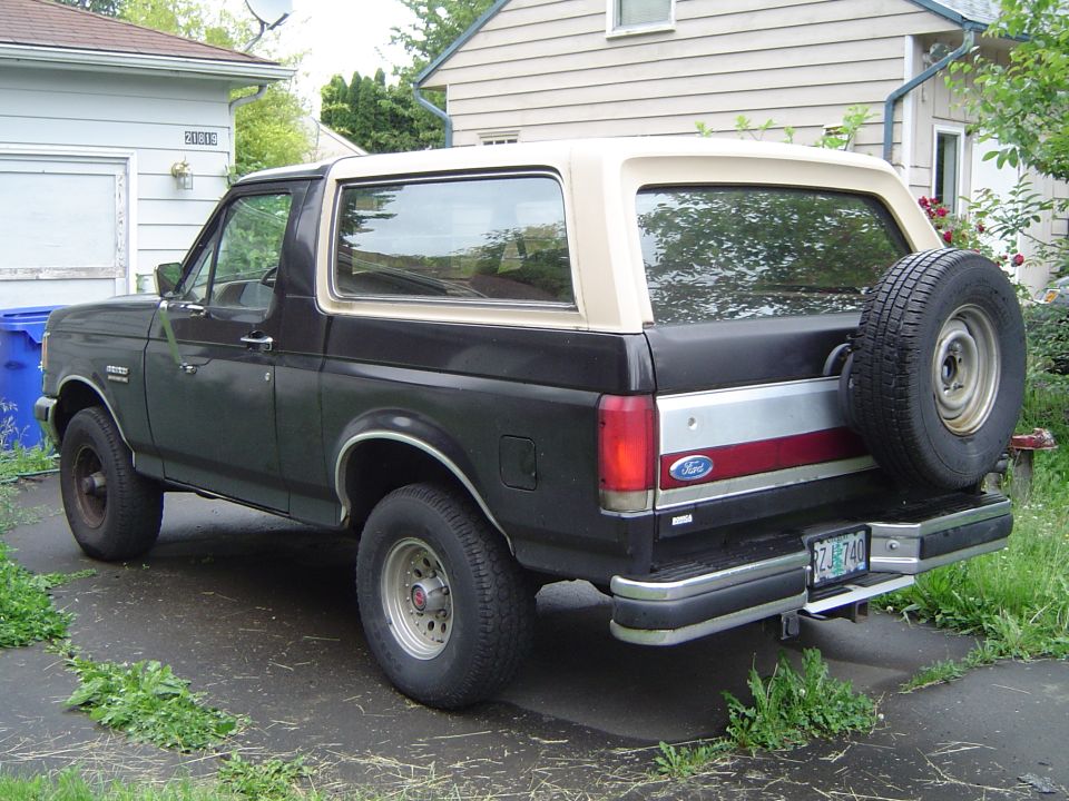 Black Ford Bronco SUV with tan top, rear spare tire, parked in driveway