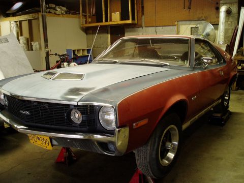 2000 Ford E350 - This American Motors AMX is undergoing some work in a garage, with its hood in primer and the rest of the body painted red.