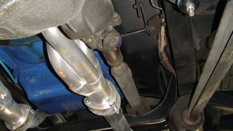 1979 Ford Bronco - Close-up of the exhaust pipes and driveshaft assembly beneath a vehicle.