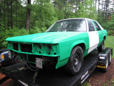 1991 Ford LTD Crown Victoria - A sedan, possibly a Ford Crown Victoria, is being transported on a trailer, with its front end partially disassembled.