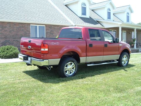 2008 Ford F-150 - A red and tan pickup truck is parked on a grassy lawn in front of a large house.