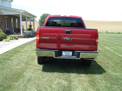 2008 Ford F-150 - Rear view of a red 2008 Ford F-150 pickup truck parked on a grassy lawn next to a house.