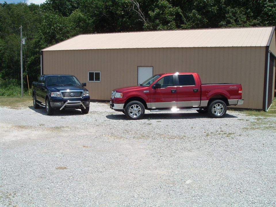 Red two-tone and dark blue Ford F-150 crew cab pickups on gravel by a barn