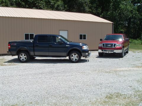 2008 Ford F-150 - Two Ford F-150 trucks are parked outside a building, one dark blue and one red.