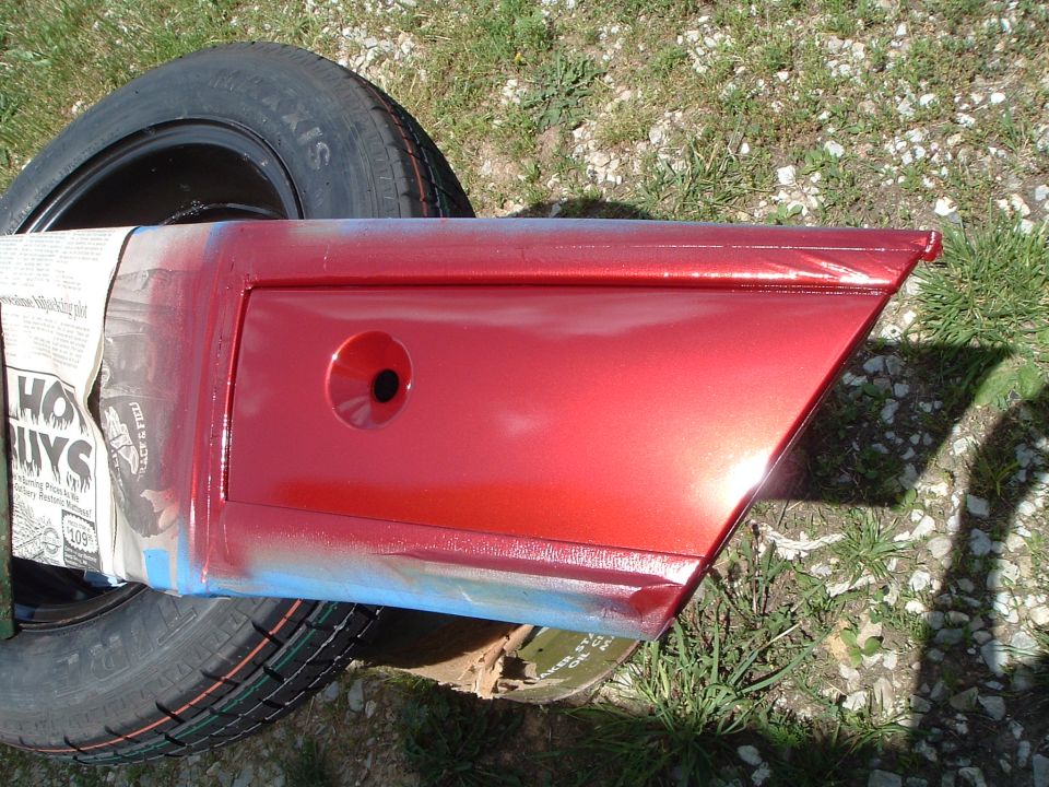 Freshly painted metallic red body panel with blue masking tape drying on a spare tire