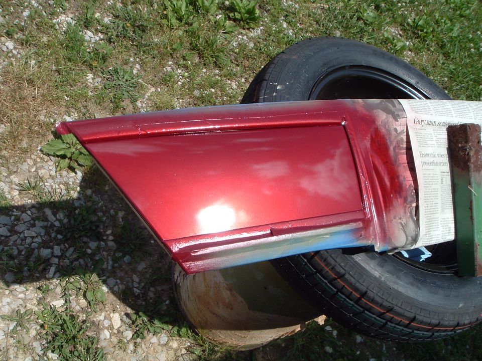 Body panel freshly sprayed metallic red drying on a tire outdoors with newspaper masking
