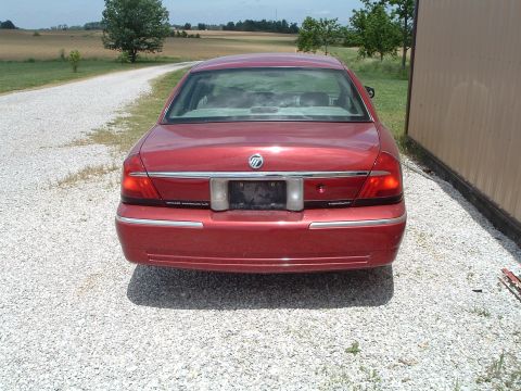 1999 Mercury Grand Marquis - Rear view of a red sedan with chrome accents, parked on a gravel surface next to a building.