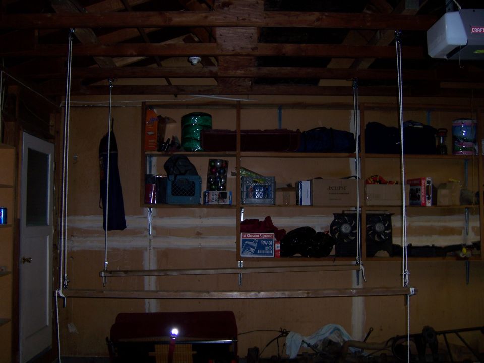 Garage interior with shelves holding various items, a door on the left, and a suspended wooden plank
