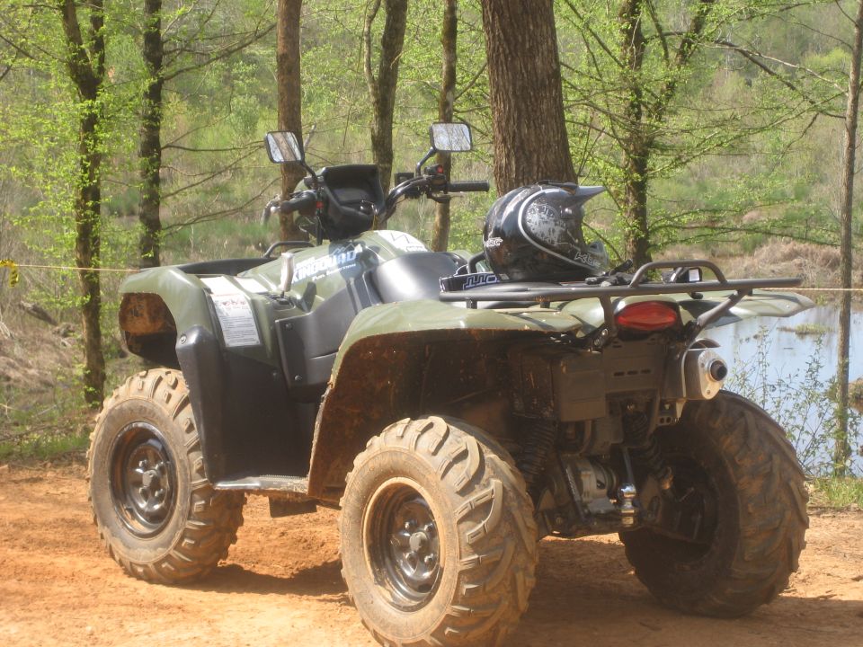 Muddy olive green Suzuki KingQuad ATV on clay trail with helmet on rear rack