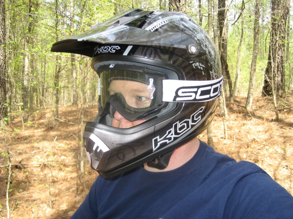 Rider wearing a black KBC motocross helmet with Scott goggles in the woods