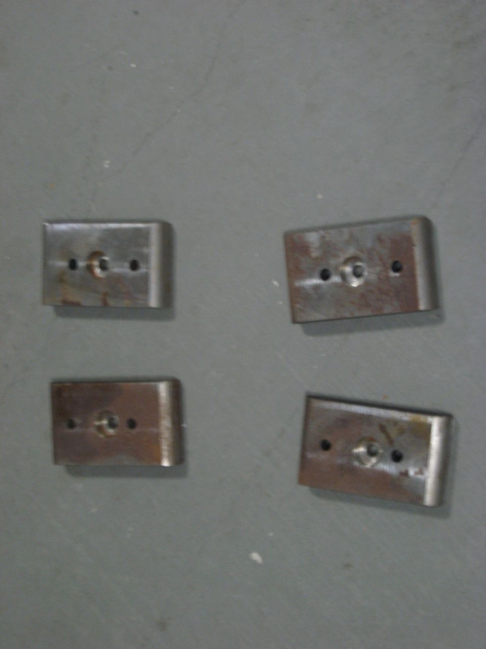 Four metal mounting brackets with holes on a gray surface
