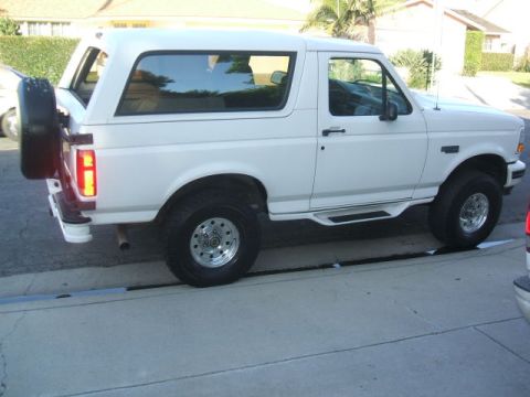 1988 Ford Bronco - The side profile of a white Ford Bronco is shown parked on a paved surface. A spare tire is mounted on the rear driver's side door, and aft…