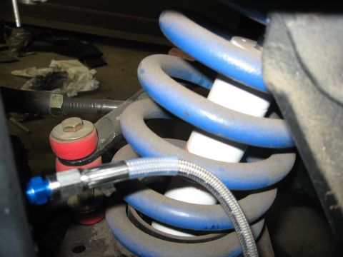 1978 Ford Mustang II - Close-up view of a blue coilover shock absorber and braided brake line, part of a vehicle's front suspension system.