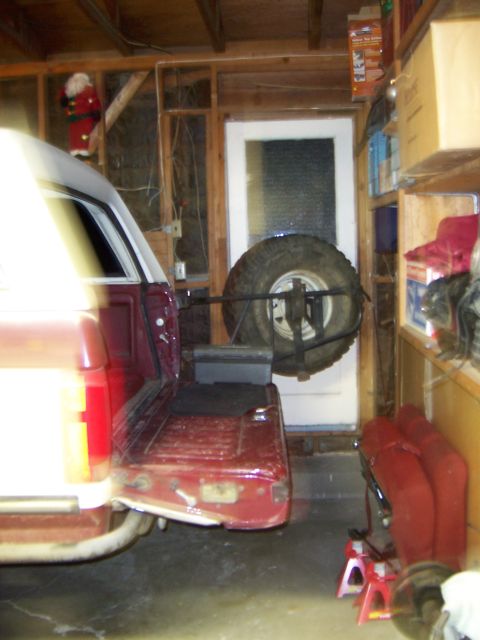 1991 Ford Bronco - A red pickup truck with a white camper shell is parked in a garage, showing its rear end and a spare tire mount.