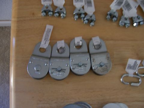 1991 Ford Bronco - Various hardware parts, including pulley blocks and cable clamps, are laid out on a wooden surface.