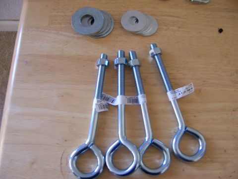 1991 Ford Bronco - Four eye bolts with nuts and washers are laid out on a wooden table, ready for use.