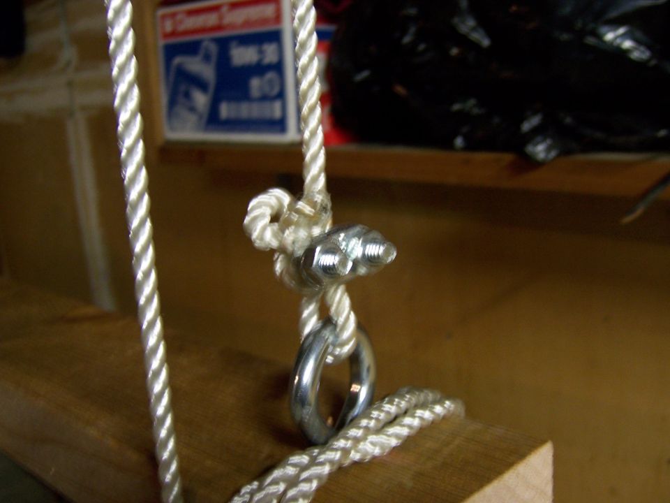 Rope tied with a knot around bolts and a metal ring, resting on a wooden beam