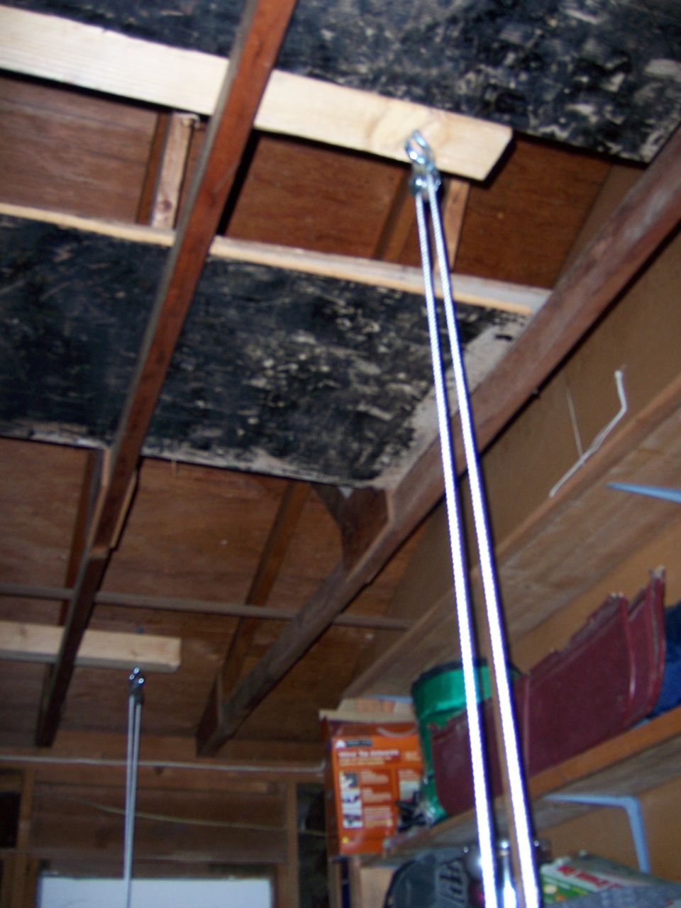 Garage ceiling with wooden beams, plywood, and a pulley system with white cables