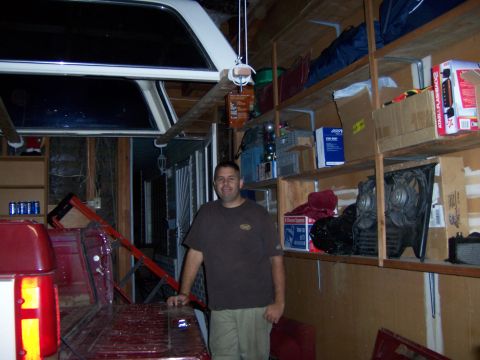 1991 Ford Bronco - A man stands in a cluttered garage beside the rear of a red pickup truck with a white camper shell.