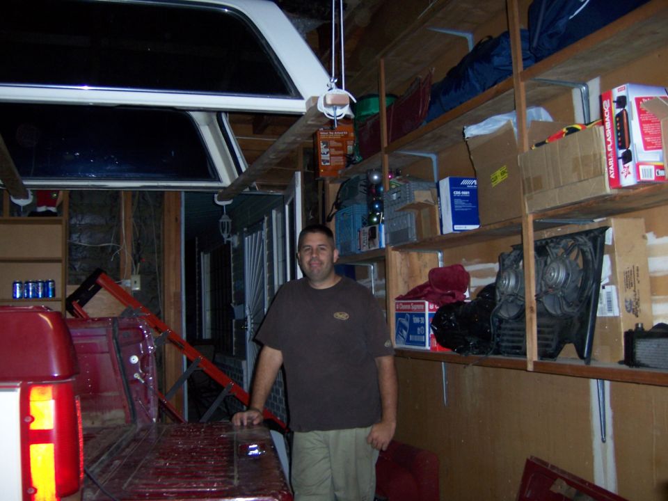 Red pickup truck bed and tailgate with a white camper shell above, viewed from the rear