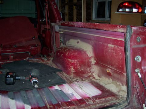 1991 Ford Bronco - The interior of a red vehicle is shown with the seats removed, revealing the floor and wheel well area.