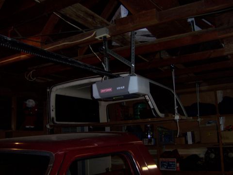 1991 Ford Bronco - A red car is parked below a white vehicle's removable top, with a garage door opener overhead.