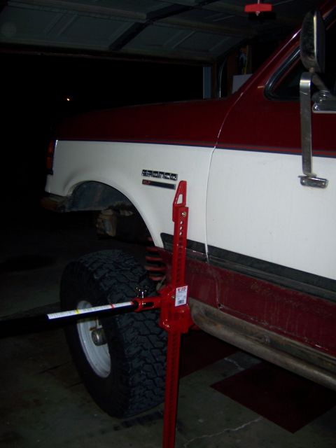 1991 Ford Bronco - A red and white Ford Bronco is shown with a high lift jack attached to the front wheel.