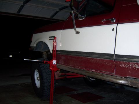 1991 Ford Bronco - A red and white 1991 Ford Bronco is shown with a Hi-Lift jack positioned next to its front wheel.