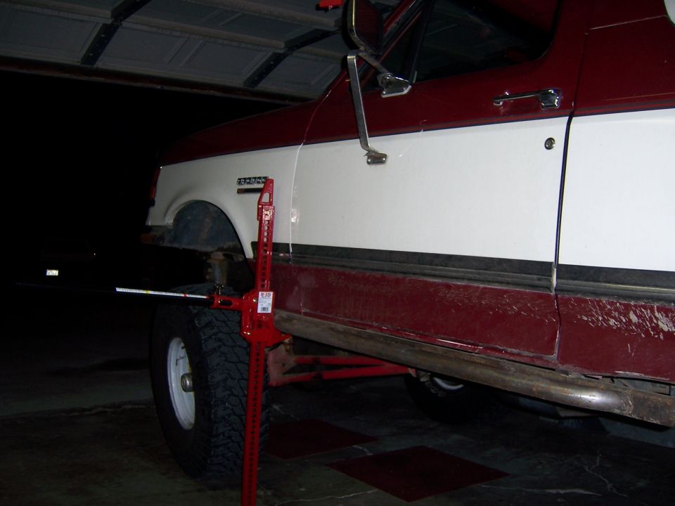 Side view of a red and white 1991 Ford Bronco with a Hi-Lift jack attached to the wheel