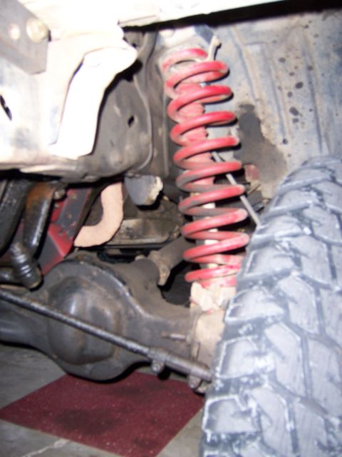 1991 Ford Bronco - Detail of vehicle suspension system, showing a red coil spring and axle components.
