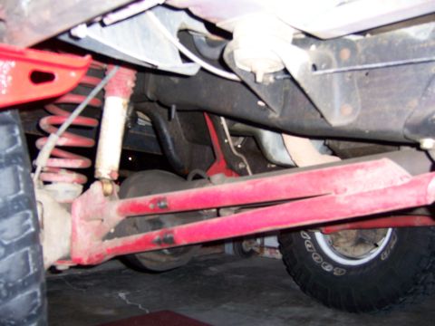1991 Ford Bronco - Close-up of the undercarriage, focusing on the suspension system and a tire. The red components suggest aftermarket modifications.