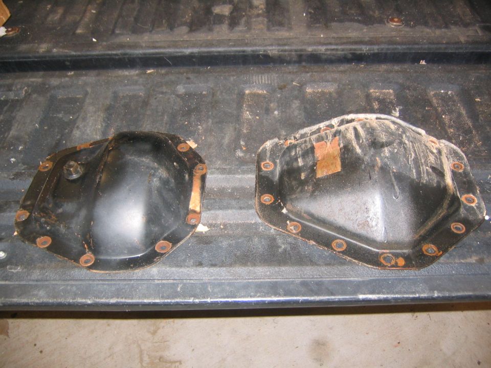 Two black differential covers with rusty bolts, resting on a truck bed