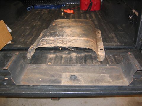 2005 Ford F-250 - A dirty, used metal part is lying in the bed of a pickup truck, possibly a skid plate or undercarriage shield.