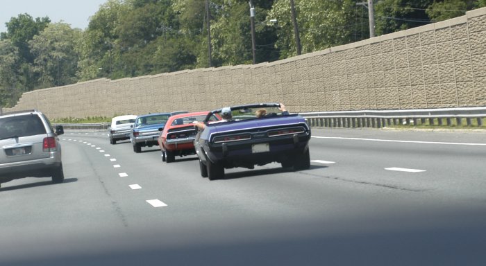 Purple convertible muscle car, rear view, on highway with other classic cars